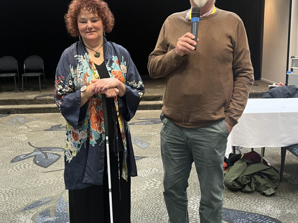 Amanda Stevens, chief executive, and Kevin Prince, President of the deafblind association of New Zealand standing to address the conference. Amanda is holding her Kevin is holding microphone