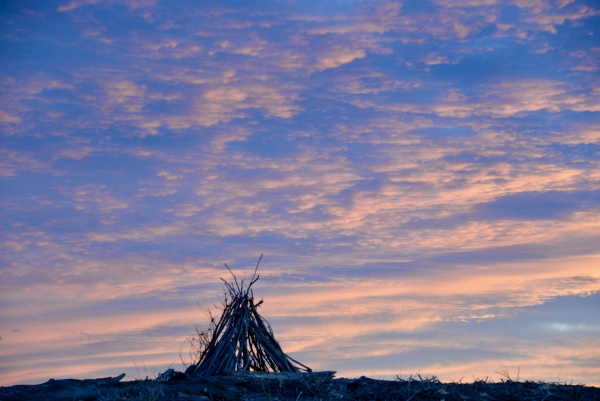 Silhouette of a driftwood teepee on a stoney beach with a colourful sunset.jpeg