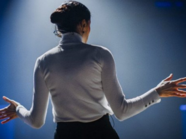 Woman in a spotlight speaks towards her audience hidden in the dark